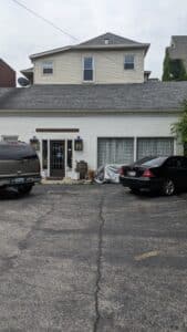 Antique shopping in Central Kentucky Day 3. Parking lot with 2 vehicles parked in front of a white building, one door, one window on the main floor 