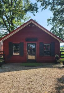 Gift Shop at Maple Hill Manor, small red building with 1 door, 2 windows. Black trim, and a peaked roof.