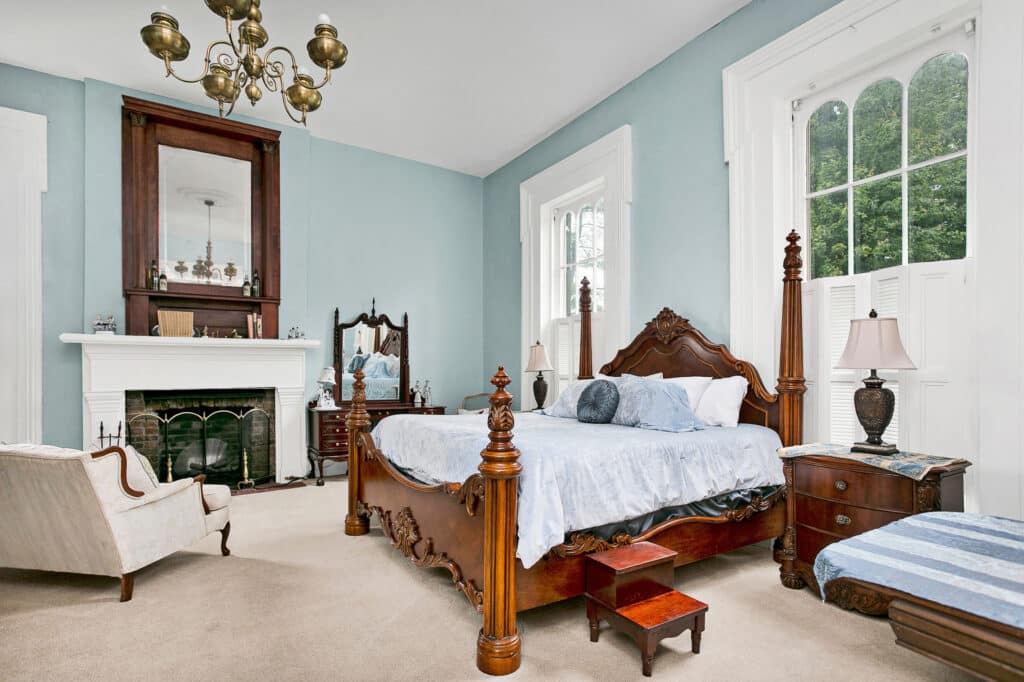 Bedroom, pale blue walls, King Poster Bed. Tall white trimmed windows, fireplace in the background